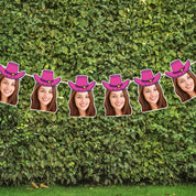 String of cutouts with faces wearing pink cowboy hats against a green hedge background