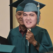 Graduating student holding a cardboard cutout of his face with a smiling man in the background.