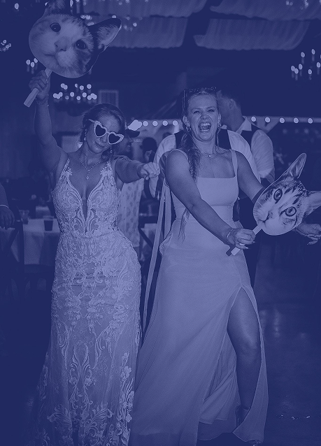 Two women in formal dresses holding animal head props at a festive event.