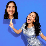 Woman in a sequin dress holding a cutout of her face against a blue background