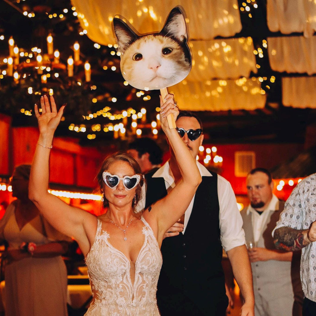 Woman holding a cat face on a stick at a festive event with blurred background