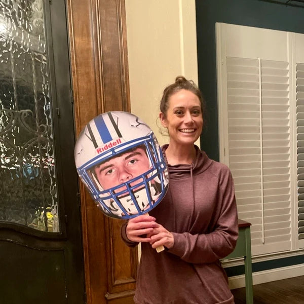 Person holding a football helmet with a face cutout in a home setting