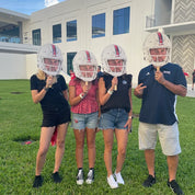 Four people holding football helmets with visors in front of their faces outdoors.