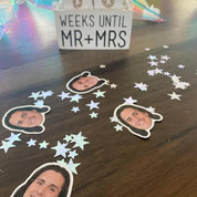 Decorative items with cut-out faces and 'Weeks Until Mr & Mrs' sign on a wooden surface.