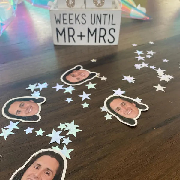 Decorative items with cut-out faces and 'Weeks Until Mr & Mrs' sign on a wooden surface.