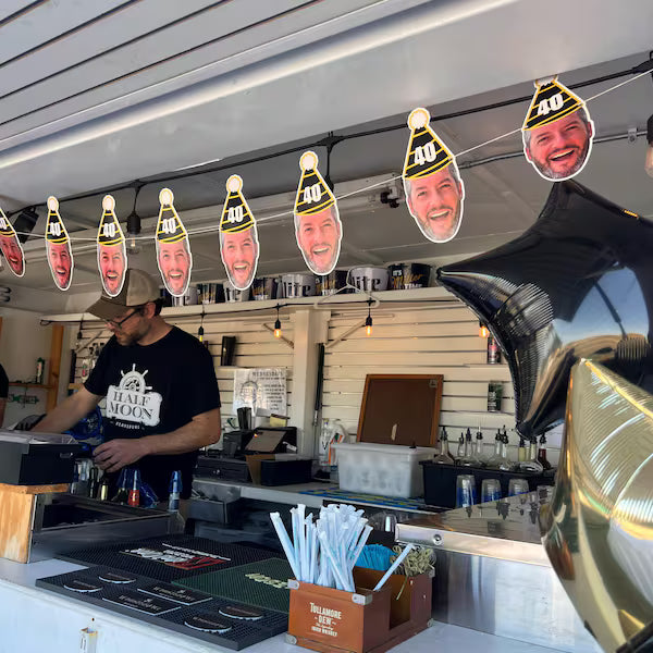 Bar setting with a person behind the bar and cutout faces hanging from the ceiling.