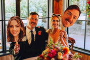 Two people holding cutout faces of a man and a woman in a celebratory setting.