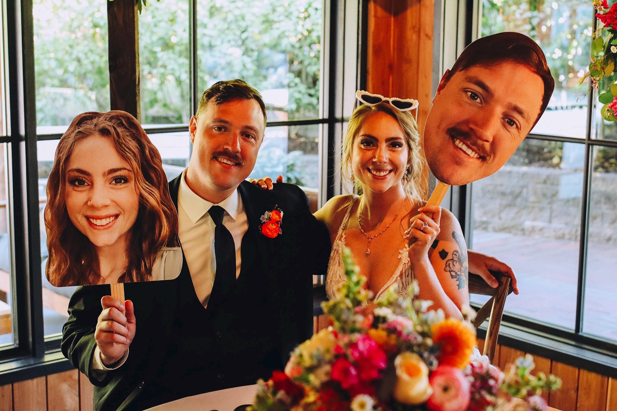 Two people holding cutout faces of a man and a woman in a celebratory setting.