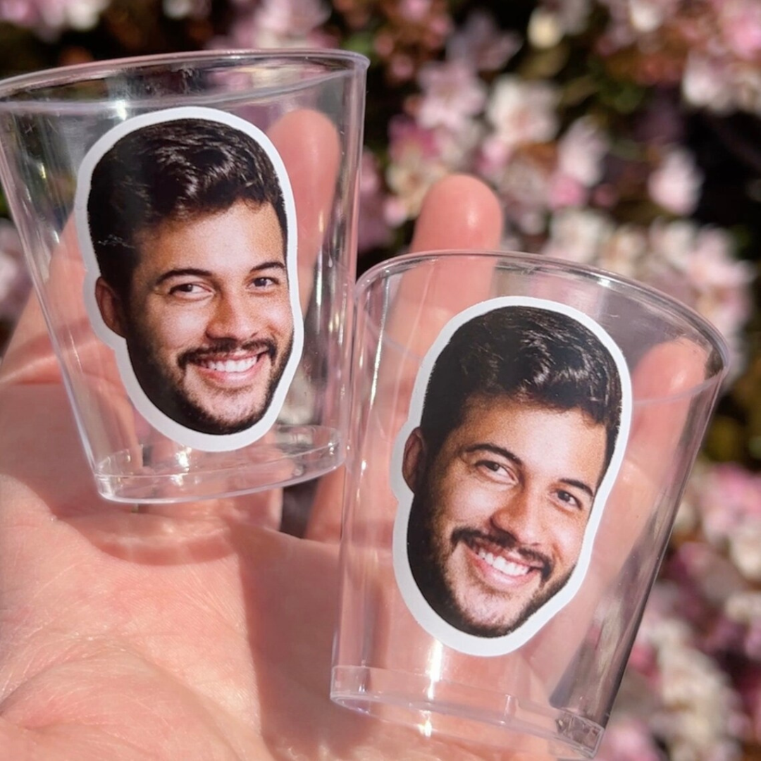 Two clear plastic cups with printed faces held against a blurred floral background